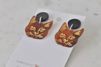 Angled view of pair of cat face drop earrings showing gold heart ear detail