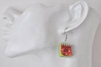Red and green calendar page earring reading December 25, shown on model's ear