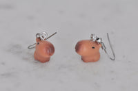 Two capybara earrings shown from behind on grey surface, showing earring hook fittings