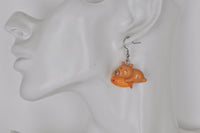 Capybara earring holding an orange fish, shown worn on ear