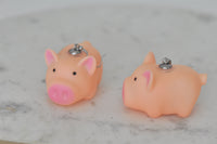 Two plastic pig earrings viewed from behind showing silver earring studs and jump rings
