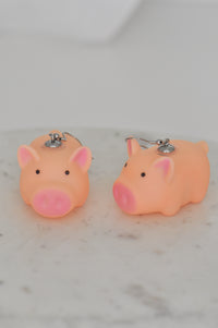 Pair of orange plastic pig drop earrings with pink ears and snout, front view on marble surface
