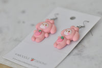 Pink bunny strawberry drop earrings lying on Kaboodle Designs branded card, angled view