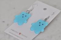 Close-up angled view of blue bear earrings showing glossy resin finish and dot face