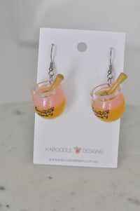 Pair of resin honey jar drop earrings labelled Wonder Honey with dippers, on card