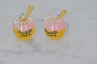 Two honey jar earrings side by side on marble surface showing amber resin colour