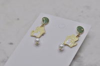 Close-up angled view of two balloon cat earrings side by side showing enamel detail and pearl beads