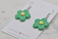 Close-up angled view of green daisy earrings showing matte resin finish and petal shape