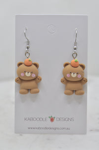Pair of resin teddy bear drop earrings with peach hats on white display card