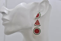 Close-up of watermelon drop earring worn on ear, showing glitter finish and seed detail