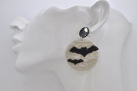 Close-up of bat and moon earring worn on ear, showing marbled grey-white finish and black bat silhouettes