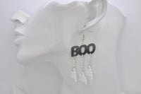 Close-up of black BOO earring with three ghost charms on chains, worn on ear