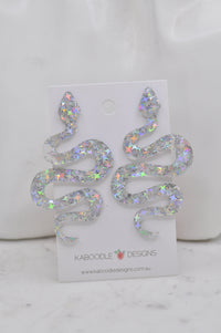 Silver glitter acrylic snake drop earrings on Kaboodle Designs card, front view