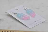 Close-up angled view of glittery angel wing earrings showing colour gradient and glossy resin finish