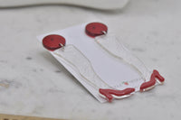 Pair of red stiletto leg earrings lying flat showing full length and shoe detail