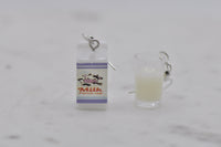 Close-up of resin milk carton and milk glass drop earrings against a white background, showing silver-tone hooks