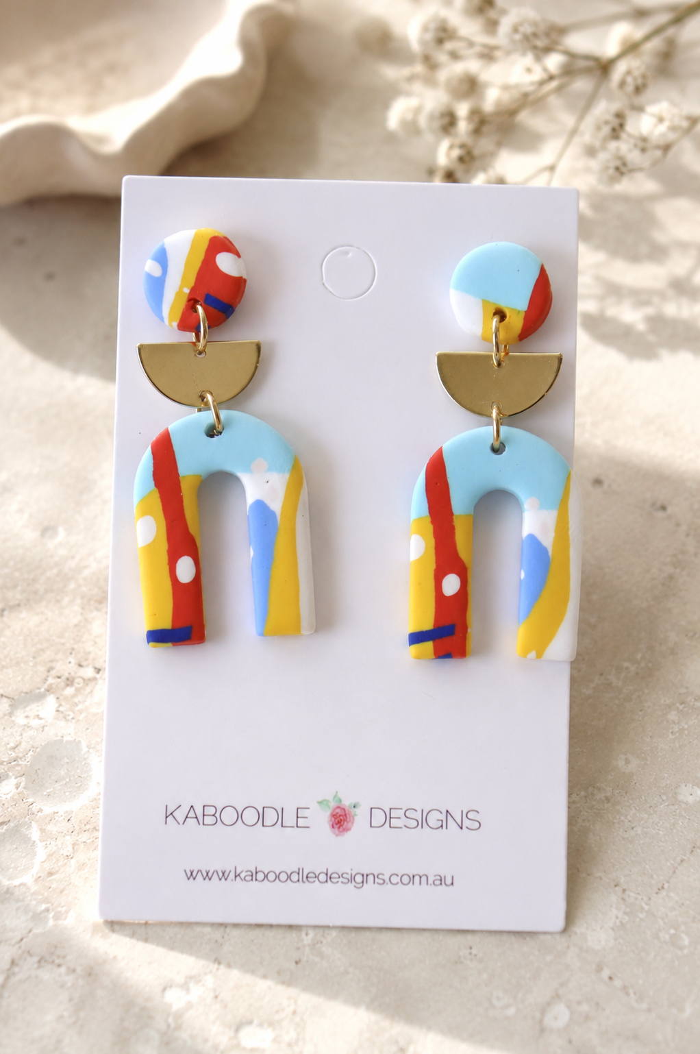 Rainbow colour-block clay horseshoe drop earrings with gold half-moon connector on display card