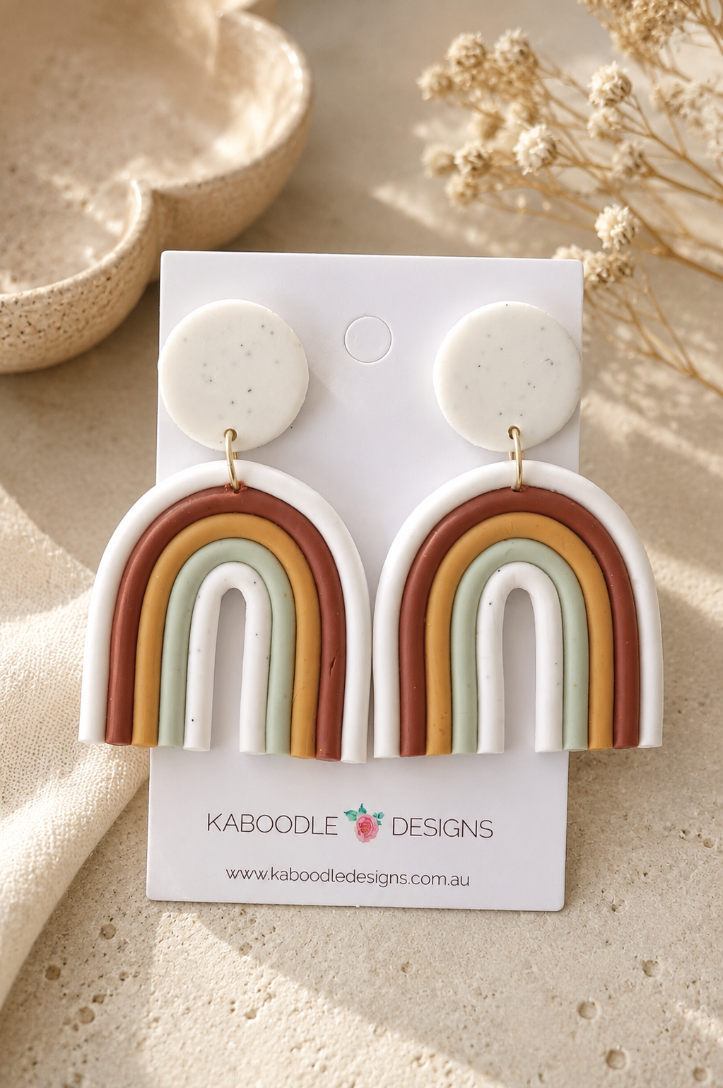Clay rainbow arch drop earrings in terracotta, mustard, sage and white on speckled white stud, shown on card