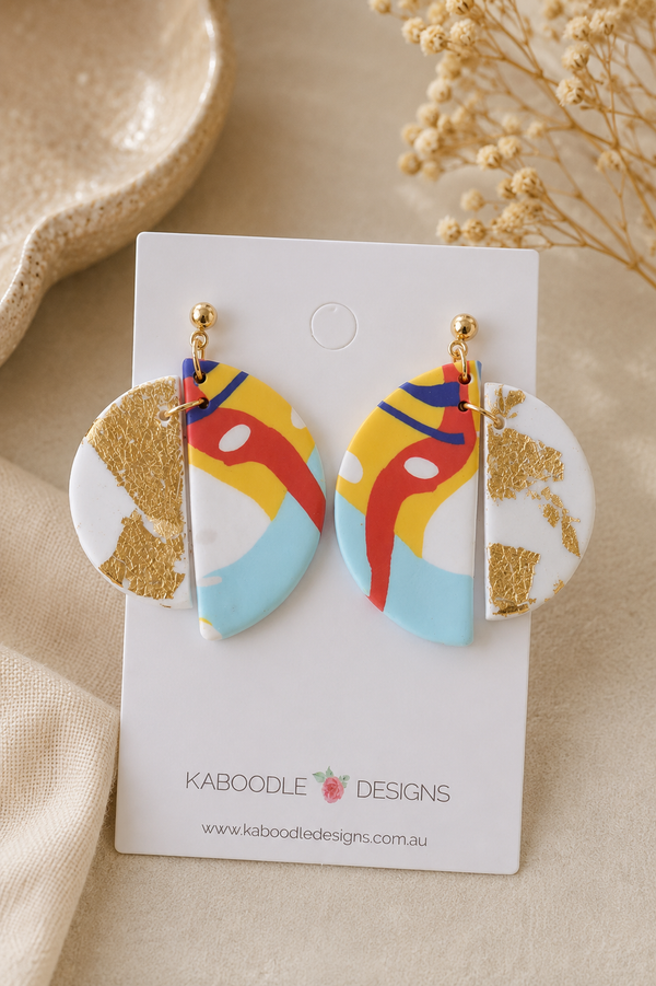 Clay drop earrings with round gold foil disc and abstract red, yellow and blue panel, on card