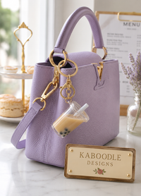 Milk tea liquid keychain clipped to lavender leather handbag with gold hardware