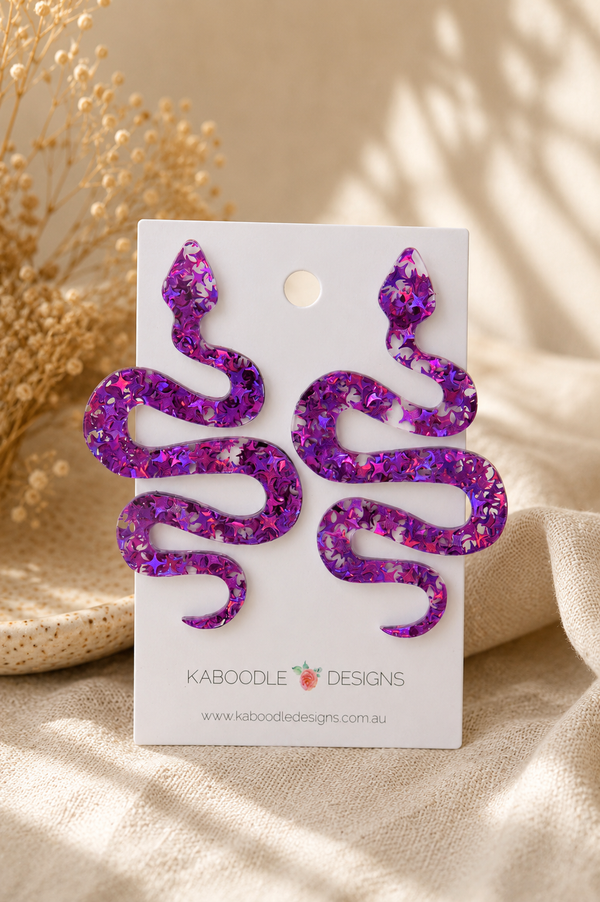 Purple glitter snake stud earrings on Kaboodle Designs card, showing coiled S-shape design