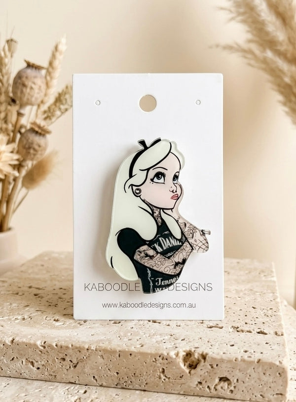 Acrylic brooch of a tattooed Alice in Wonderland character with pale hair, inked arms and a dark graphic tank top design