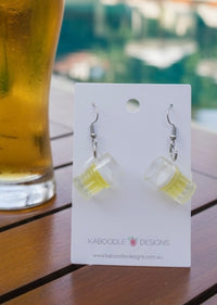 Resin beer mug drop earrings on Kaboodle Designs card, shown beside a glass of beer