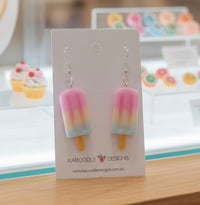 Popsicle-shaped resin earrings on display card with cupcake decor in background