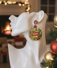 Close-up of one gold bauble earring with red Merry Christmas script and green trees, worn on a model ear form