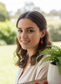 Close-up of model wearing a single red strawberry drop earring outdoors