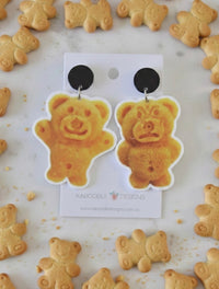 Pair of Tiny Teddy biscuit earrings on card, black stud tops, glossy bear shapes surrounded by real biscuits
