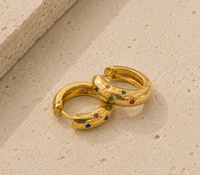 Pair of gold huggie hoop earrings with colourful star-set gems, close-up on textured surface