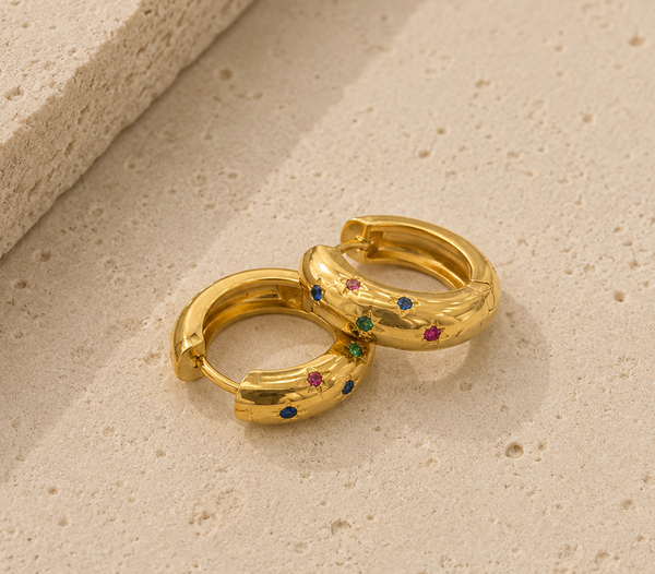 Pair of gold huggie hoop earrings with colourful star-set gems, close-up on textured surface