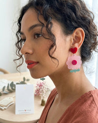 Close-up of pink flower heart earring worn on model's ear, showing red heart stud and layered acrylic flower drop