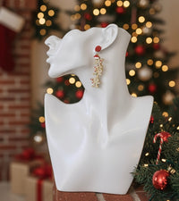 Gingerbread earring shown on ear against a blurred Christmas tree with fairy lights