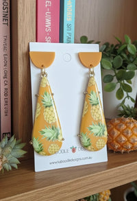 Mustard-yellow resin teardrop earrings with pineapple print on white display card