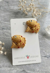 Two gold polymer clay koi fish stud earrings on a Kaboodle Designs card, facing opposite directions