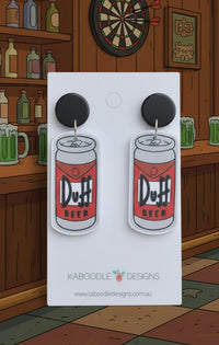 Acrylic Duff Beer can drop earrings with black stud tops on white card, bar backdrop