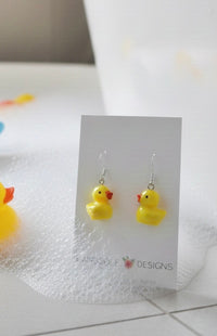 Pair of rubber ducky earrings on card against a bubbly bathtub-style background