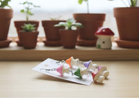 Mushroom earrings laid flat on card packaging with terracotta plant pots and ceramic mushroom in background