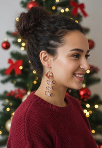 Woman wearing Santa sleigh reindeer drop earrings styled with a red jumper and Christmas tree backdrop