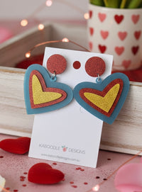 Layered acrylic heart earrings with red glitter stud, blue heart outline and yellow glitter centre on card backing