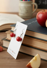 Side view of red apple drop earrings on display card leaning against stacked books