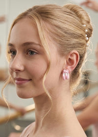 Pink ballet shoe stud earring worn on model's ear, close-up side view