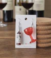 Red wine bottle and glass novelty drop earrings displayed on a white card