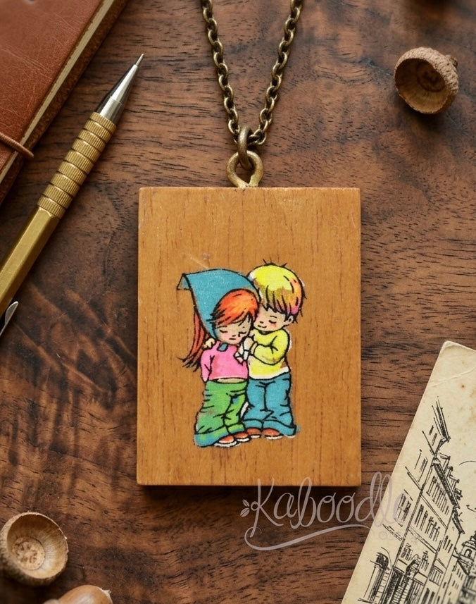 Rectangular wooden pendant necklace with illustrated couple embracing under a blue umbrella