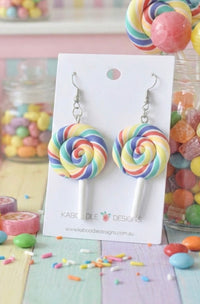 Pair of rainbow swirl lollipop polymer clay earrings on white Kaboodle Designs card with candy background