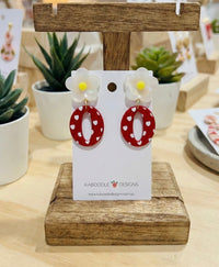 Pearly white daisy stud earrings with red heart-print acrylic hoop drops on display card