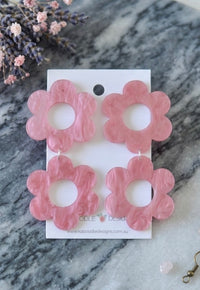 Two pairs of pink marbled acrylic daisy drop earrings on a card, flat lay with dried flowers