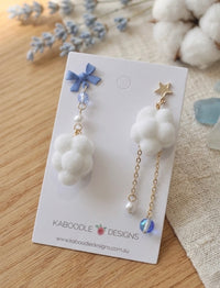 Mismatched cloud earrings on card, one with blue bow and cloud, one with gold star and chain